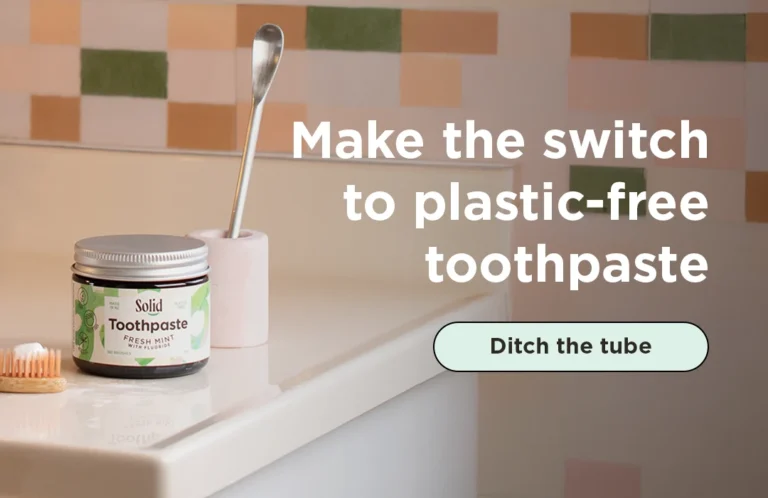 Toothpaste in a jar on bathroom sink with toothpaste scoop and toothbrush
