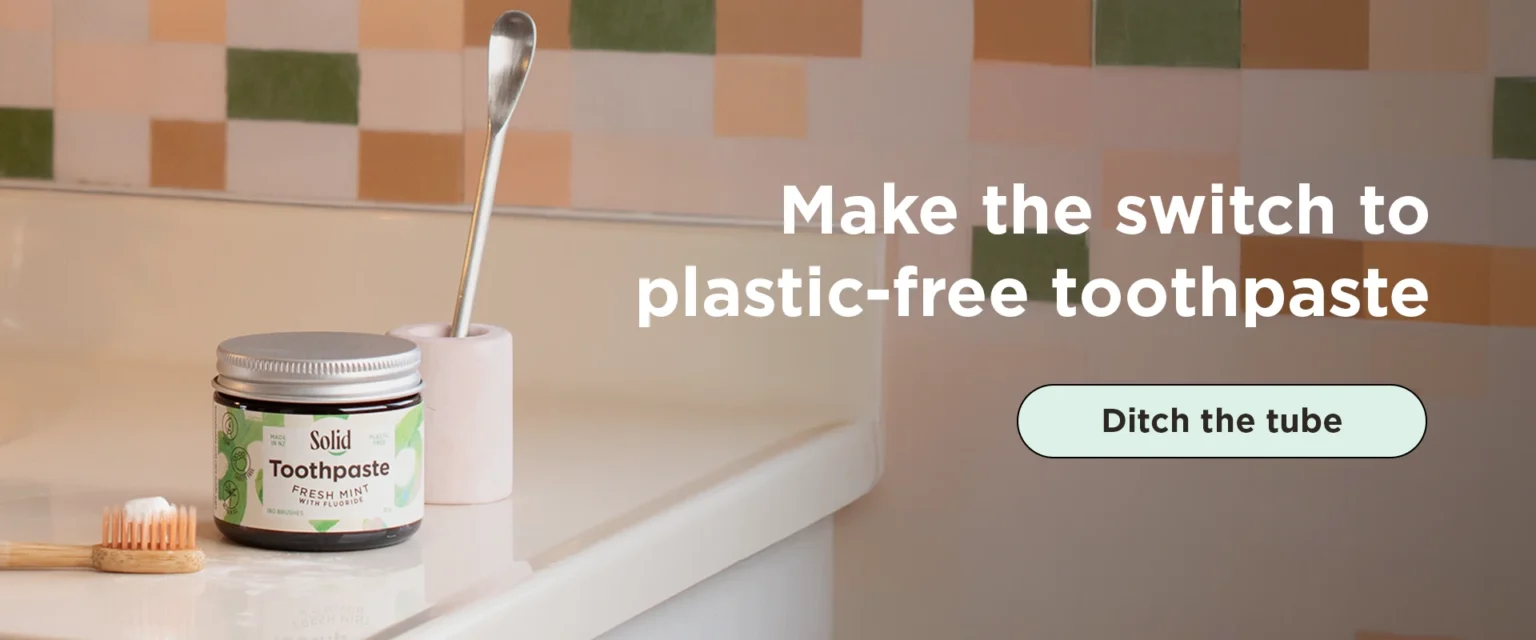 Toothpaste in a jar on bathroom sink with toothpaste scoop and toothbrush